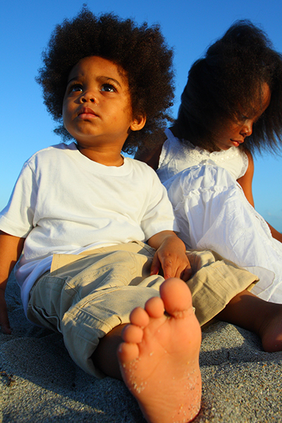 young boy and girl wearing white clothes and sitting in sand