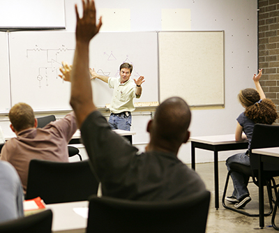 adult students with raised hands face instructor at white board