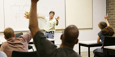 adult students with raised hands face instructor at white board